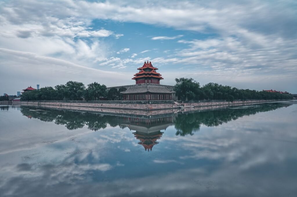 Serene reflection of the Forbidden City on a tranquil lake in Beijing, under a blue sky.